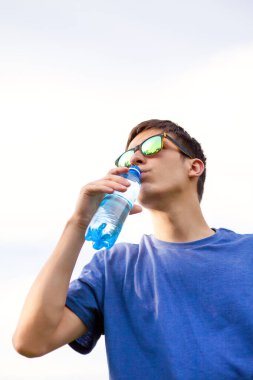 Genç adam Gökyüzü Arkaplanında Saf Su İçiyor