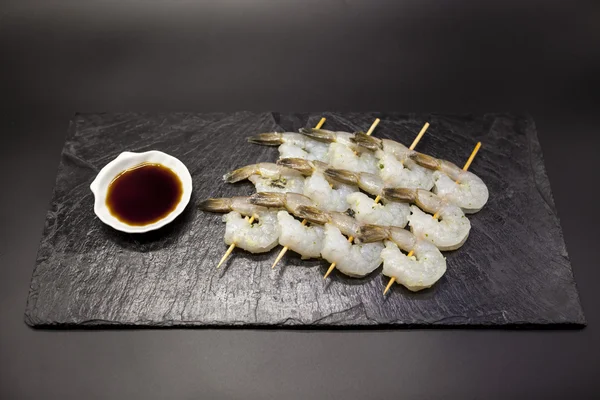 Tiger shrimps shish kebabs of teriyaki on a stone plate with soy sauce.