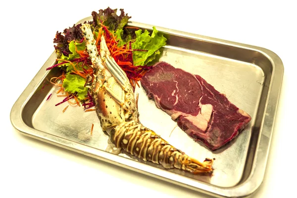 Set for surf and turf a fresh crude lobster and a juicy piece of a marble stake on a tray.