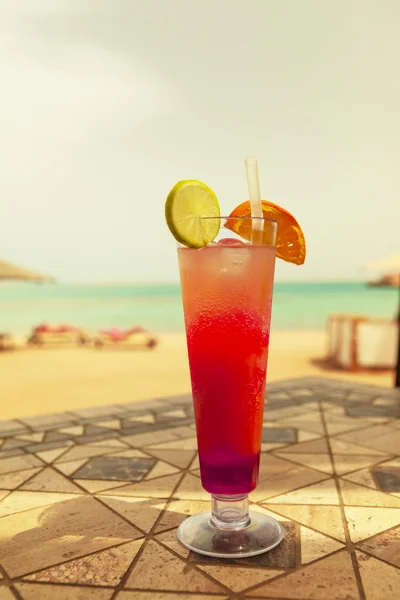 Tequila sunrise cocktail with ice on a table against the sea — Stock Photo, Image