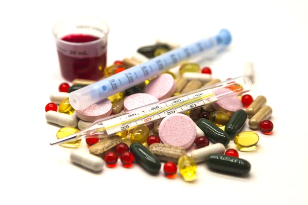 Diferentes píldoras, medicamentos con medicamentos con una jeringa y con termómetro sobre fondo blanco . — Foto de Stock