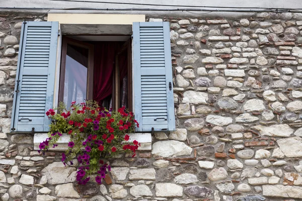 Vieja ventana con persianas abiertas con flores en el alféizar de la ventana en la pared de piedra. Pueblo italiano — Foto de Stock