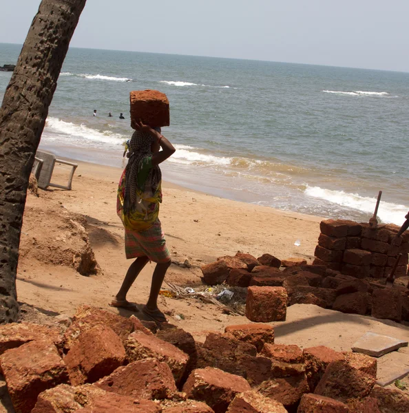 The Indian woman in a sari stones for building on the head on a beach. India Goa — Stock Photo, Image