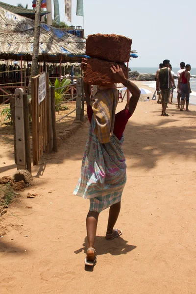 The Indian woman in a sari stones for building on the head on a beach. India Goa — Stock Photo, Image