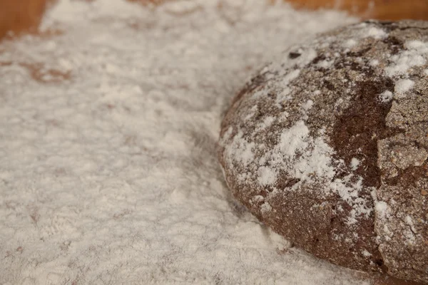 Dark homemade bread lies on flour on a wooden tray. — Stockfoto