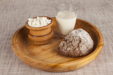 Ev yapımı peynir, bir bardak süt, kahverengi ekmek bir ahşap tepsi.
