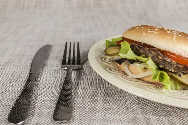 Čerstvý hamburger s kotleta mramorované hovězího a čerstvé zeleniny na talíři s vidličkou a nožem — Stock fotografie