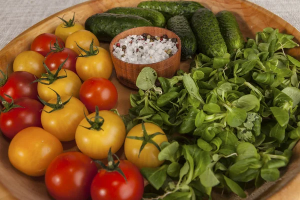 Tomates y pepinos cherry rojos y amarillos frescos, cebollas en una bandeja de madera de estilo rústico . — Foto de Stock