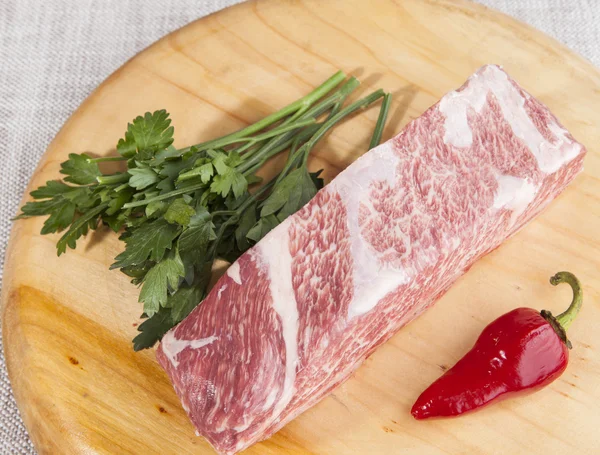 A piece of fresh marbled beef, chili pepper, parsley, ribs lie on a wooden tray — Stock Fotó