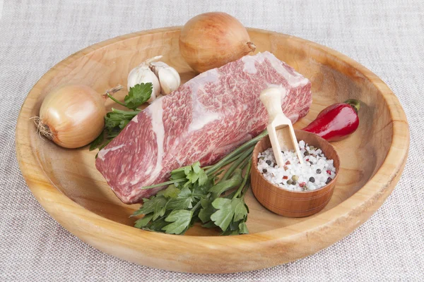A piece of fresh marbled beef, chili pepper, parsley, onion, garlic, ribs lie on a wooden tray — Zdjęcie stockowe