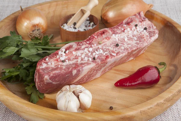 A piece of fresh marbled beef, chili pepper, parsley, onion, garlic, ribs lie on a wooden tray — Stok fotoğraf