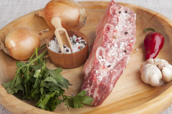 A piece of fresh marbled beef, chili pepper, parsley, onion, garlic, ribs lie on a wooden tray — Zdjęcie stockowe