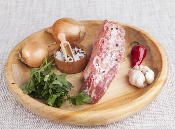 A piece of fresh marbled beef, chili pepper, parsley, onion, garlic, ribs lie on a wooden tray — Φωτογραφία Αρχείου