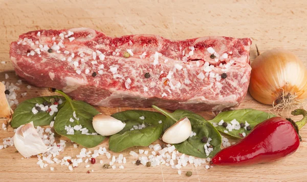 Close-up piece of fresh marbled beef, chili pepper, parsley, onion, garlic, ribs lie on a wooden tray — Φωτογραφία Αρχείου