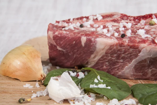 Close-up piece of fresh marbled beef, chili pepper, parsley, onion, garlic, ribs lie on a wooden tray — Zdjęcie stockowe