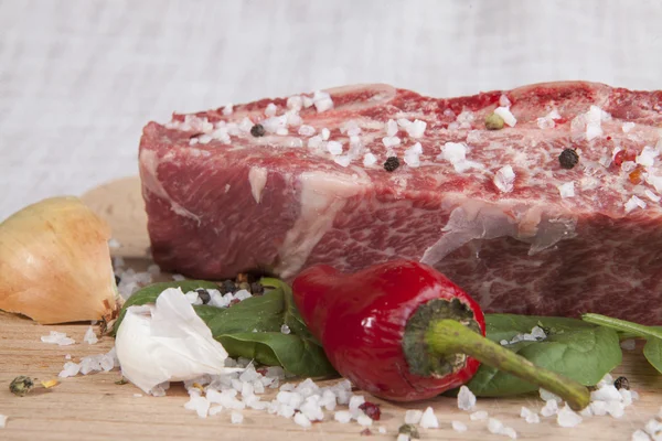 Pedaço de close-up de carne fresca marmorizada, pimenta, salsa, cebola, alho, costelas jazem em uma bandeja de madeira — Fotografia de Stock