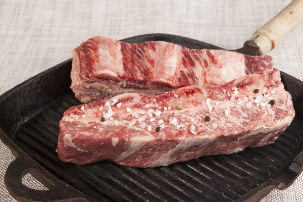 Close-up of two pieces of fresh marbled beef with sea salt and black pepper, on a cast-iron grill pan — Zdjęcie stockowe