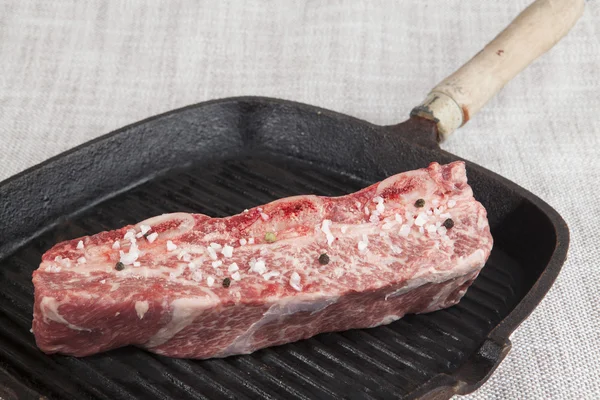 Close-up piece of fresh marbled beef with sea salt and black pepper,  on a cast-iron grill pan — Stock Fotó