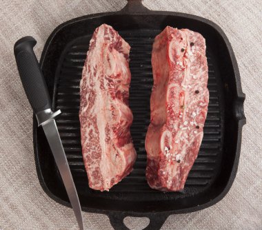Close-up of two pieces of fresh marbled beef with sea salt and black pepper, knife  on a cast-iron grill pan