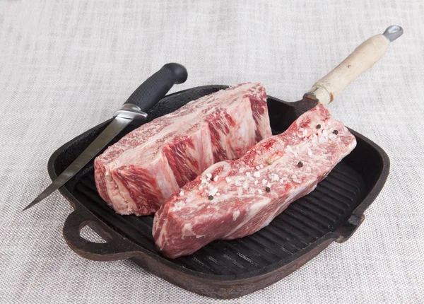 Close-up of two pieces of fresh marbled beef with sea salt and black pepper, knife  on a cast-iron grill pan — Zdjęcie stockowe
