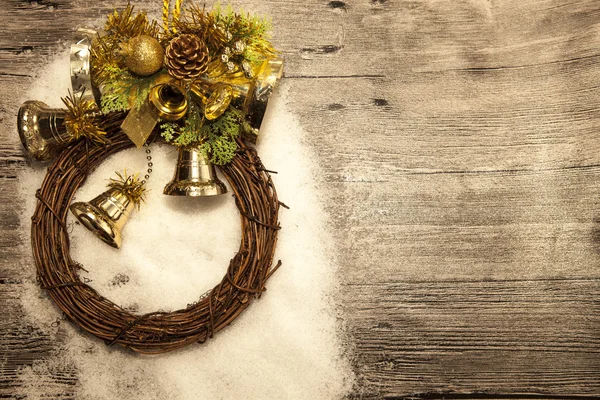 Třpytivé zlaté vánoční koule, zvonky, věnec a hvězda na dřevěném pozadí se sněhem . — Stock fotografie