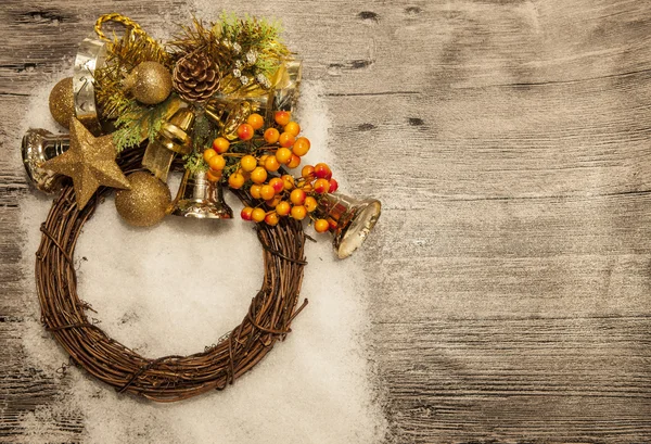 Glittering gold Christmas balls, bells,wreath, and star on wooden background with snow . — Stock Photo, Image