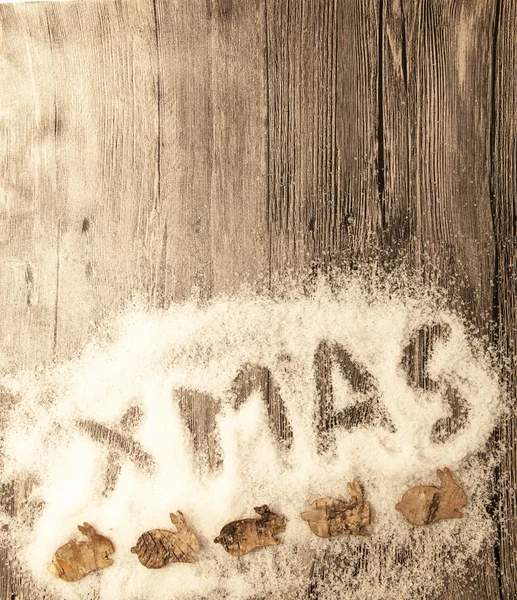 Christmas card with the inscription xmas with christmas small rabbits from birch bark  in the snow on a wooden background — Stock fotografie