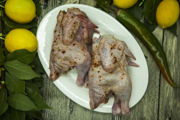 Два сырых свежих цыпленка на фарфоровой тарелке с лимоном и чили на деревянном фоне — стоковое фото