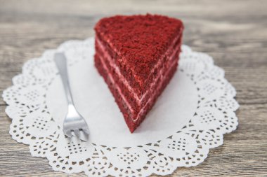 Fresh tasty sweet piece of  red velvet cake, on a white napkin and a dessert fork on a wooden background clipart