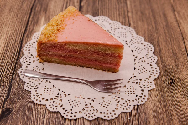 Friss finom édes darab rózsaszín torta a fehér szalvéta és desszert villát a fából készült háttér — Stock Fotó