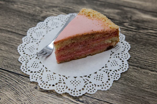 Pedaço doce saboroso fresco de bolo rosa em um guardanapo branco e um garfo de sobremesa em um fundo de madeira — Fotografia de Stock