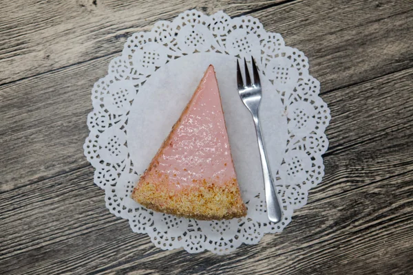 Pedaço doce saboroso fresco de bolo rosa em um guardanapo branco e um garfo de sobremesa em um fundo de madeira — Fotografia de Stock