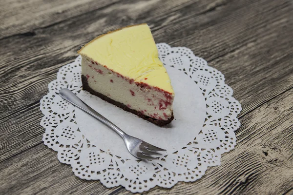 Pedaço doce saboroso fresco de bolo de queijo em um guardanapo branco e um garfo de sobremesa em um fundo de madeira — Fotografia de Stock