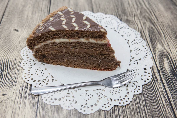 Fresco y sabroso pedazo de pastel de chocolate en una servilleta blanca y un tenedor de postre sobre un fondo de madera —  Fotos de Stock