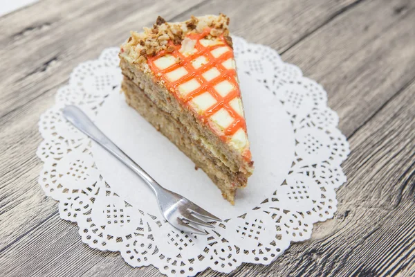 Pedaço doce saboroso fresco de bolo de cenoura em um guardanapo branco e um garfo de sobremesa em um fundo de madeira — Fotografia de Stock