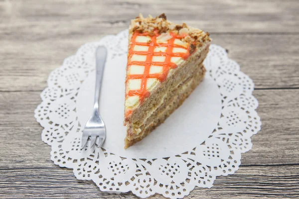 Pedaço doce saboroso fresco de bolo de cenoura em um guardanapo branco e um garfo de sobremesa em um fundo de madeira — Fotografia de Stock