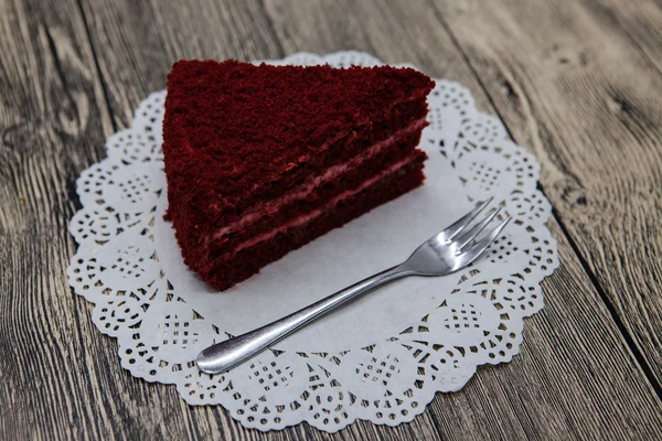 Pedaço doce saboroso fresco de bolo de veludo vermelho, em um guardanapo branco e um garfo de sobremesa em um fundo de madeira — Fotografia de Stock