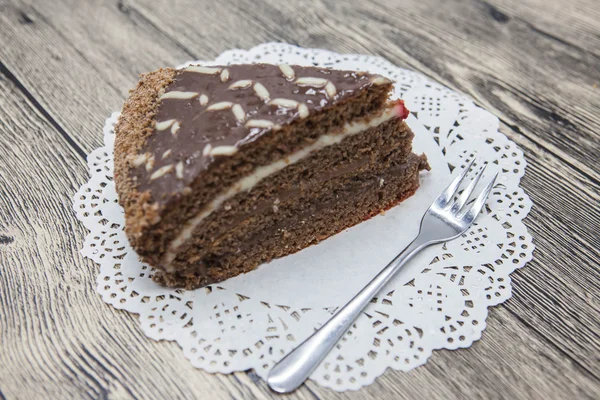 Fresco y sabroso pedazo de pastel de chocolate en una servilleta blanca y un tenedor de postre sobre un fondo de madera —  Fotos de Stock