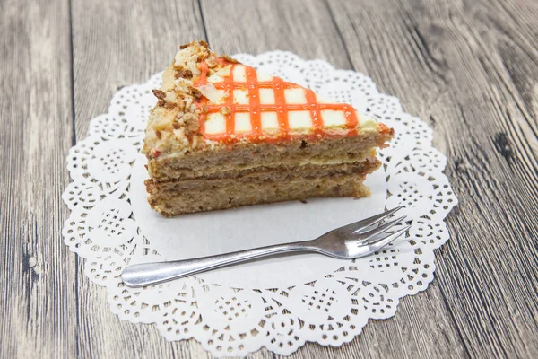 Pedaço doce saboroso fresco de bolo de cenoura em um guardanapo branco e um garfo de sobremesa em um fundo de madeira — Fotografia de Stock