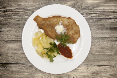 Petite Wiener schnitzel with boiled potatoes and ketchup. Served on a white porcelain plate on a wooden background.