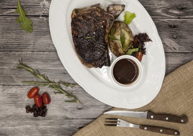 Sebze ve barbekü soslu mermer dana eti nden Ribeye biftek. Çatal ve bıçak ile siyah taş bir tabak üzerinde servis .