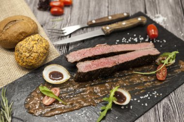 Sebze ve barbekü soslu mermer dana eti nden Ribeye biftek. Çatal ve bıçak ile siyah taş bir tabak üzerinde servis .