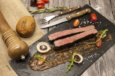 Sebze ve barbekü soslu mermer dana eti nden Ribeye biftek. Çatal ve bıçak ile siyah taş bir tabak üzerinde servis .