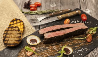 Sebze ve barbekü soslu mermer dana eti nden Ribeye biftek. Çatal ve bıçak ile siyah taş bir tabak üzerinde servis .