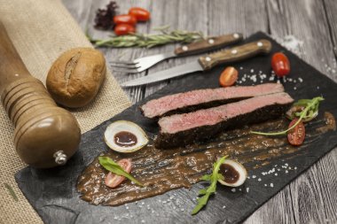 Sebze ve barbekü soslu mermer dana eti nden Ribeye biftek. Çatal ve bıçak ile siyah taş bir tabak üzerinde servis .