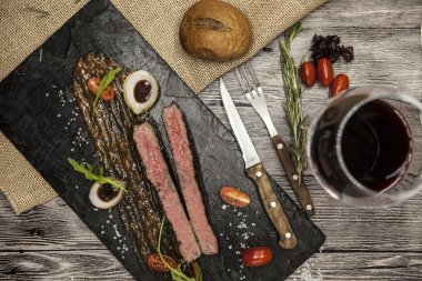 Ribeye steak from marble beef meat with vegetables and barbecue sauce. Served on a plate of black stone with fork and knife and wine.