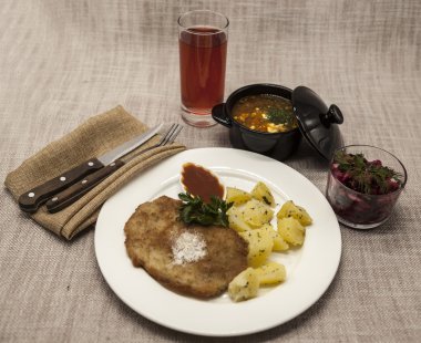 Business lunch : Petite Wiener schnitzel with boiled potatoes and ketchup. Served on a white porcelain plate with fork and knife on a wooden background. Beet  salad and tomato, red pepper soup, sauce 