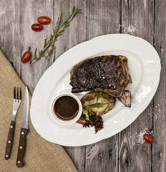 Ribeye steak de viande de bœuf de marbre avec des légumes et sauce barbecue. Servi sur une assiette de pierre noire avec fourchette et couteau  . — Photo