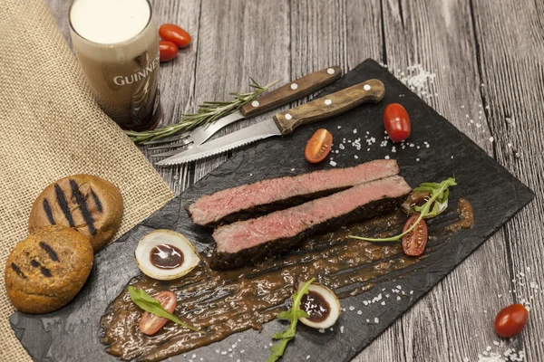 Ribeye steak from marble beef meat with vegetables and barbecue sauce. Served on a plate of black stone with fork and knife . — Stock Photo, Image