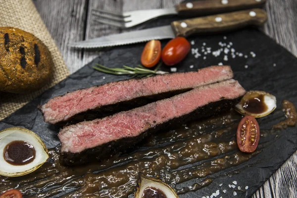 Sebze ve barbekü soslu mermer dana eti nden Ribeye biftek. Çatal ve bıçak ile siyah taş bir tabak üzerinde servis . — Stok fotoğraf